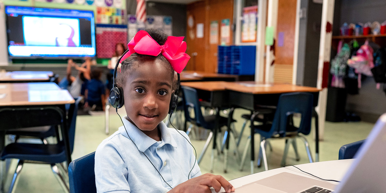 A smiling student using the laptop in class and wearing a headset.